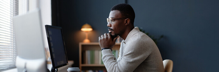 Website header shot of thoughtful Black office worker using desktop computer at working desk...