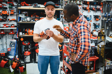The seller helps the buyer choose a screwdriver in a hardware store.