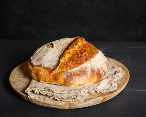 A homebaked artisan sourdough bread with scoring leaves on a round cutting board with a tea towel.