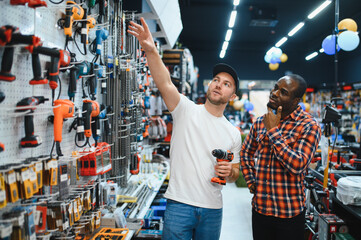 Buying a drill or screwdriver. A consultant in a hardware store advises a male customer on the...