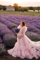 Fototapeta premium a pregnant woman in a pink dress holds a bouquet of lavender in her hands and stands in a lavender field