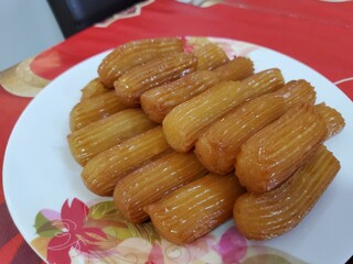 Golden Tulumba pastries, glistening with syrup, arranged on a rustic plate. A delectable Middle...