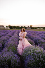 a pregnant woman in a pink dress put her hand on her stomach in a lavender field
