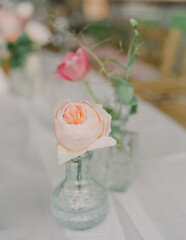 Charming floral arrangement featuring peony and pink buds in glass vases on a wooden table setting
