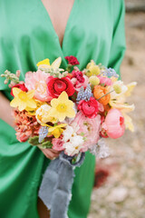 Vibrant bridal bouquet held by woman in green gown amidst natural setting during outdoor wedding celebration