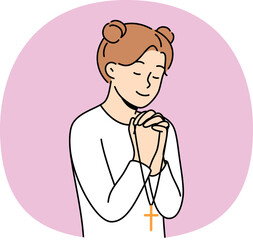 Little girl reads prayer, crossing palms near chest and holding christian cross in hands. Happy pre-teen child praying, feeling involved in catholicism and christian religion at early age