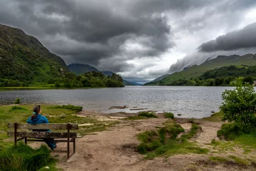 Woman On Bench Looking Over Lake Loch Shiel At Glenfinnan Monument On The Road To The Isles In Lochaber In Scotland, UK