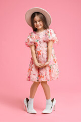 Stylish little girl wearing oversized high heeled shoes on pink background