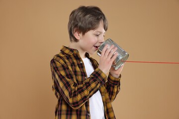 Boy using tin can telephone on beige background