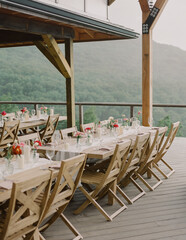 Elegant outdoor dining setup featuring tables adorned with flowers on a scenic mountain backdrop at sunset