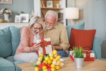 Couple joyfully celebrating a special occasion with a surprise gift while sitting on a couch in a cozy living room