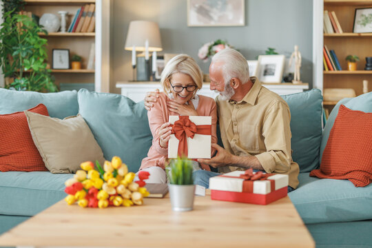 Couple sharing a joyful moment while opening a gift in a cozy living room decorated with flowers and warm colors