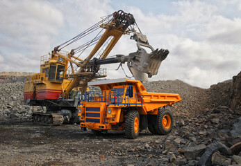Digger loading dump truck with iron ore. Big yellow mining truck hauling rock in coal mine. No AI tools