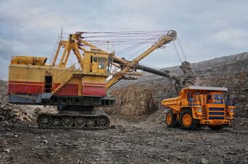 Industrial excavator loading ore into big yellow truck of quarry. Iron ore mining. No AI tools