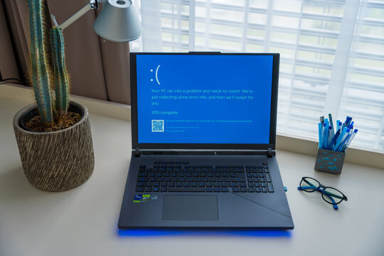 Prague, Czech Republic - September 11, 2024: A laptop displays the blue screen of death while in use at a home office desk, signaling a system crash. The workspace is organized with a cactus and lamp.