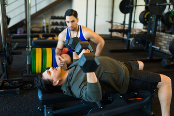 Fitness trainer supervising a client performing dumbbell exercises on a bench in a gym, focusing on proper form and technique