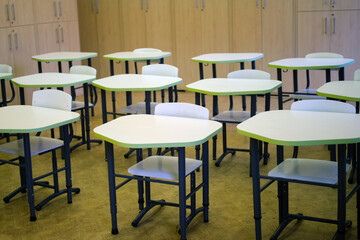 Empty classroom with modern student desks and chairs arranged in rows. Educational facility interior with wooden cabinets in the background. School learning environment concept