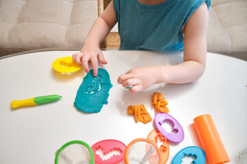 Child crafting with colorful modeling clay and shape cutters on a white table. Close-up photography of creative activity materials. Craft and play concept for design and print. Kid aged three year