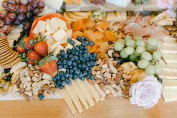 Colorful spread of fruits, cheeses, nuts, and garnishes on a wooden table for a gathering or event