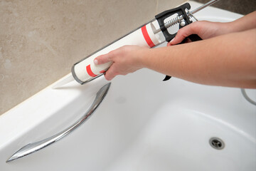 Hand applying sealant to bathtub corner using caulking gun. Home renovation and bathroom...