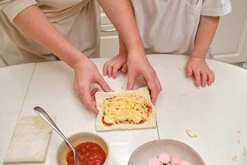 A parent and her toddler are spending quality time together while baking in the kitchen. The mom and her child are smiling while making a delicious pizza from scratch.