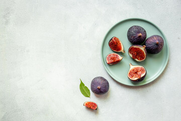 Plate with fresh ripe figs whole and slices with green leaves. Top view