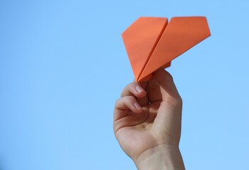 Woman with handmade paper plane against blue sky outdoors, closeup. Space for text
