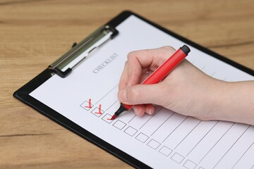 Woman filling Checklist with marker at wooden table, closeup