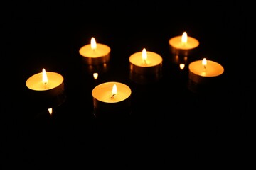 Many burning candles in darkness, closeup view