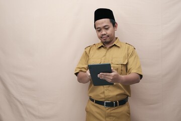 Handsome government worker man wearing khaki uniform holding tablet or tab while smiling. PNS and...