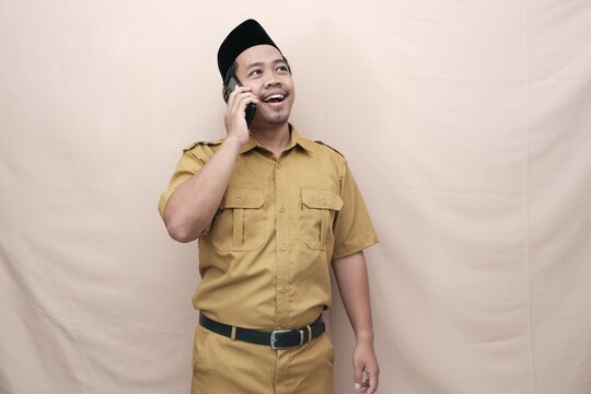 Smiling Indonesian government worker man wearing khaki uniform while talking on the phone. PNS ASN civil servant concept.