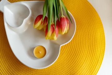 Tulips and a white ceramic stand and a candle on an orange carpet.