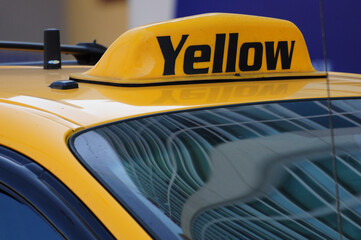 Close-up of a bright yellow taxi roof sign reflecting urban life and city vibes.