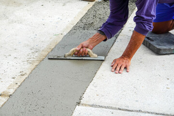 Hands using a trowel to smooth fresh wet concrete