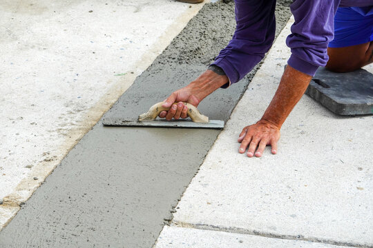 Hands using a trowel to smooth fresh wet concrete