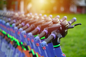 Electric scooters stands in row on sidewalk of city street for the rent. A lot of parked e-scooters.