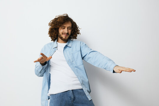 Happy young man dancing in a casual outfit with curly hair, showcasing joy against a minimalistic white background Perfect for lifestyle and happiness themes