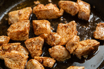 Chicken fillet pieces are fried in a frying pan in sauce and spices