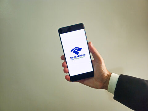 Person holding smartphone with Receita Federal - Meu imposto de Renda (Brazilian Federal Revenue Department) logo on screen. Income tax declaration in Brazil.