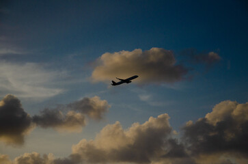 Silhouette of a plane flying through a partly cloudy blue sky.