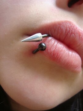 piercing on plump lips. The face of a girl with lip piercings. Gothic, lip thorn, puncture
