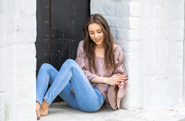 Portrait of a young beautiful brunette girl in blue jeans posing in a stone arch