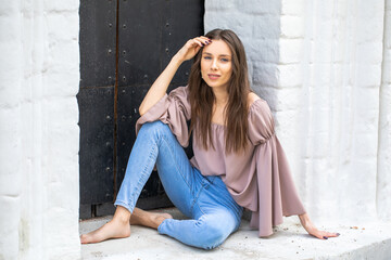 Portrait of a young beautiful brunette girl in blue jeans posing in a stone arch