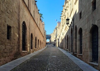 Photo of the Street of the Knights, a historic cobblestone path in Rhodes' Old Town, showcasing Gothic architecture with towering stone buildings, intricate carvings, and ornate facades.