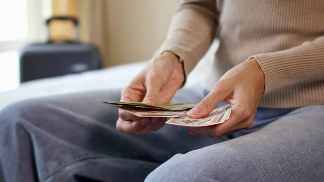Close up view of a female traveler hands counting Nepalese rupee cash money while packing a suitcase for a holiday trip. Preparing money and luggage for vacation. Concept of travel expenses in Nepal.