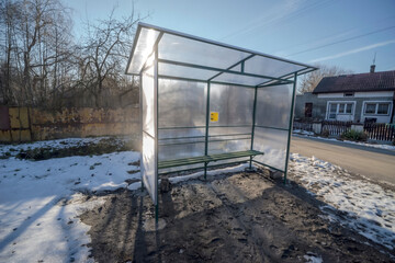 Przystanek autobusowy ze stali i pleksi w małym miasteczku (Denkówek) w słoneczny zimowy dzień. Przystanek autobusowy z płaskim dachem i przezroczystymi panelami. Zawiera prostą ławkę wspartą na ramie © Grzegorz