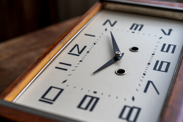 A table clock with a wooden case and an analog dial.The clock is striking.Vintage background.