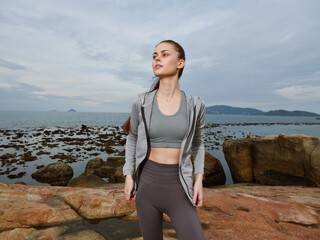 Young athletic woman in activewear on rocky beach, showcasing confidence and determination against...