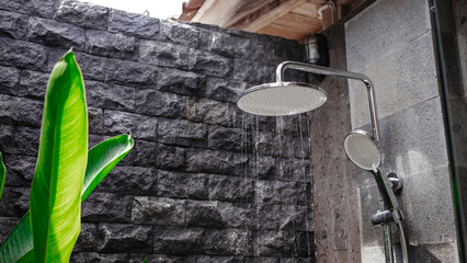 Tropical outdoor shower against the background of a gray brick wall. Stylish shower room with a green palm tree background