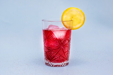 Elegant red cocktail with lemon slice on light background. The drink is filled with ice cubes, enhancing its cool and refreshing appeal.